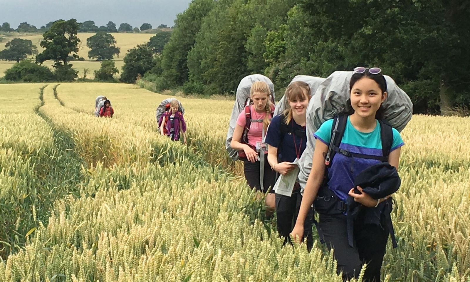 Bronze DofE students, girls group, walking through a wheat field with rucksacks