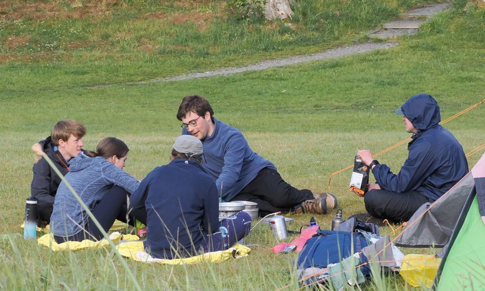 Group of young people sitting around their campsite eating tea