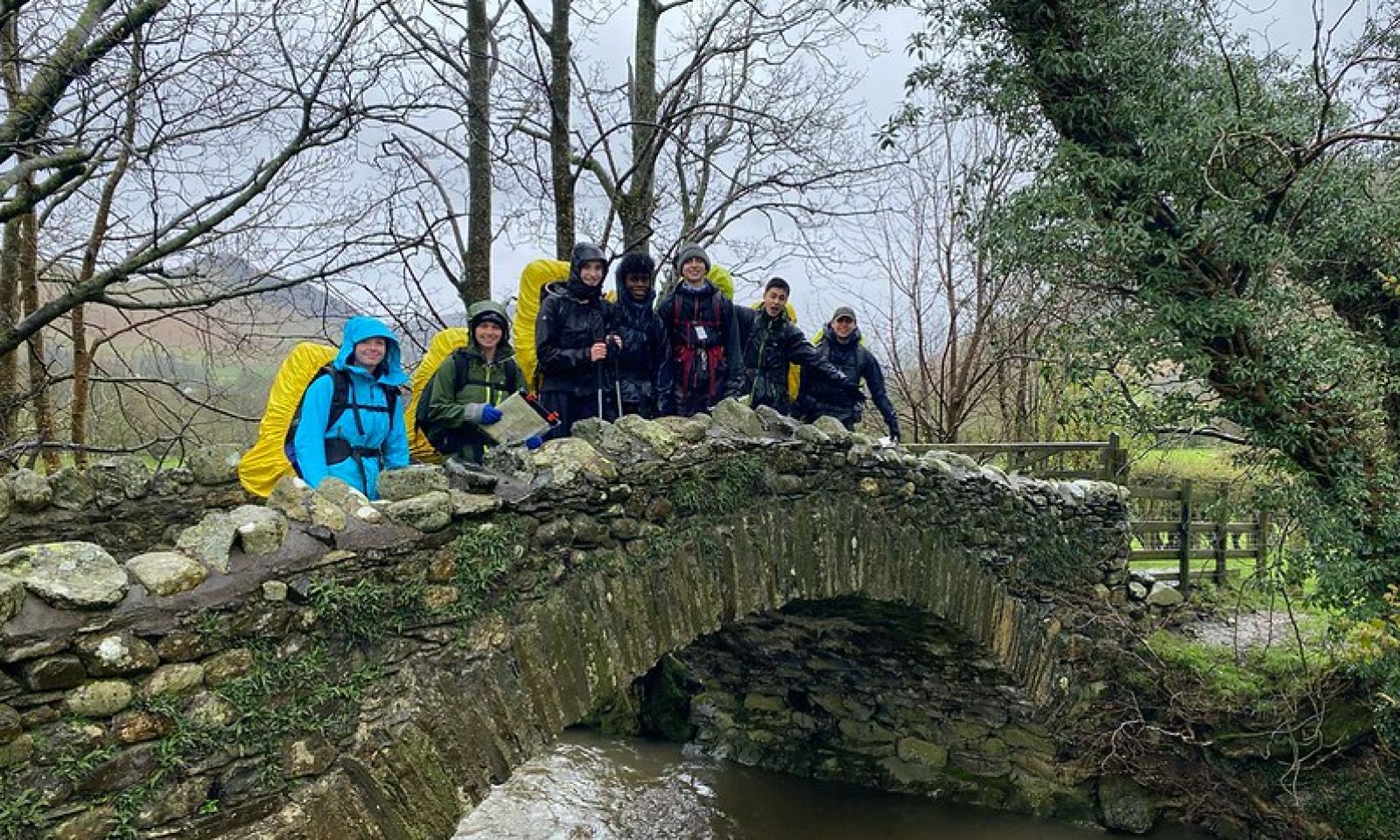 DofE silver award students crossing a bridge in the Lake District with their full rucksacks, blue sky