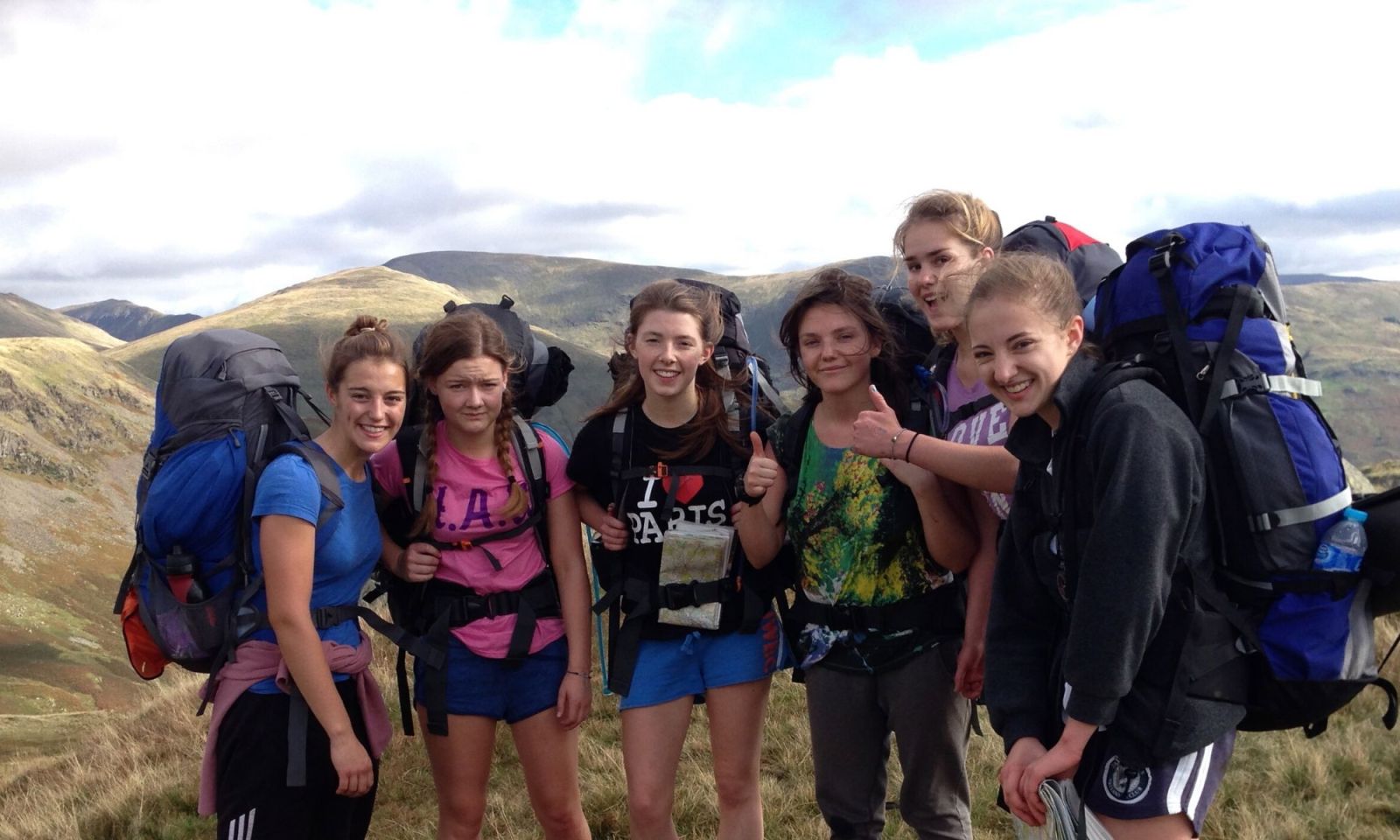 Group of girls DofE group in the hills, smiling, with their full rucksacks and mountains in the background