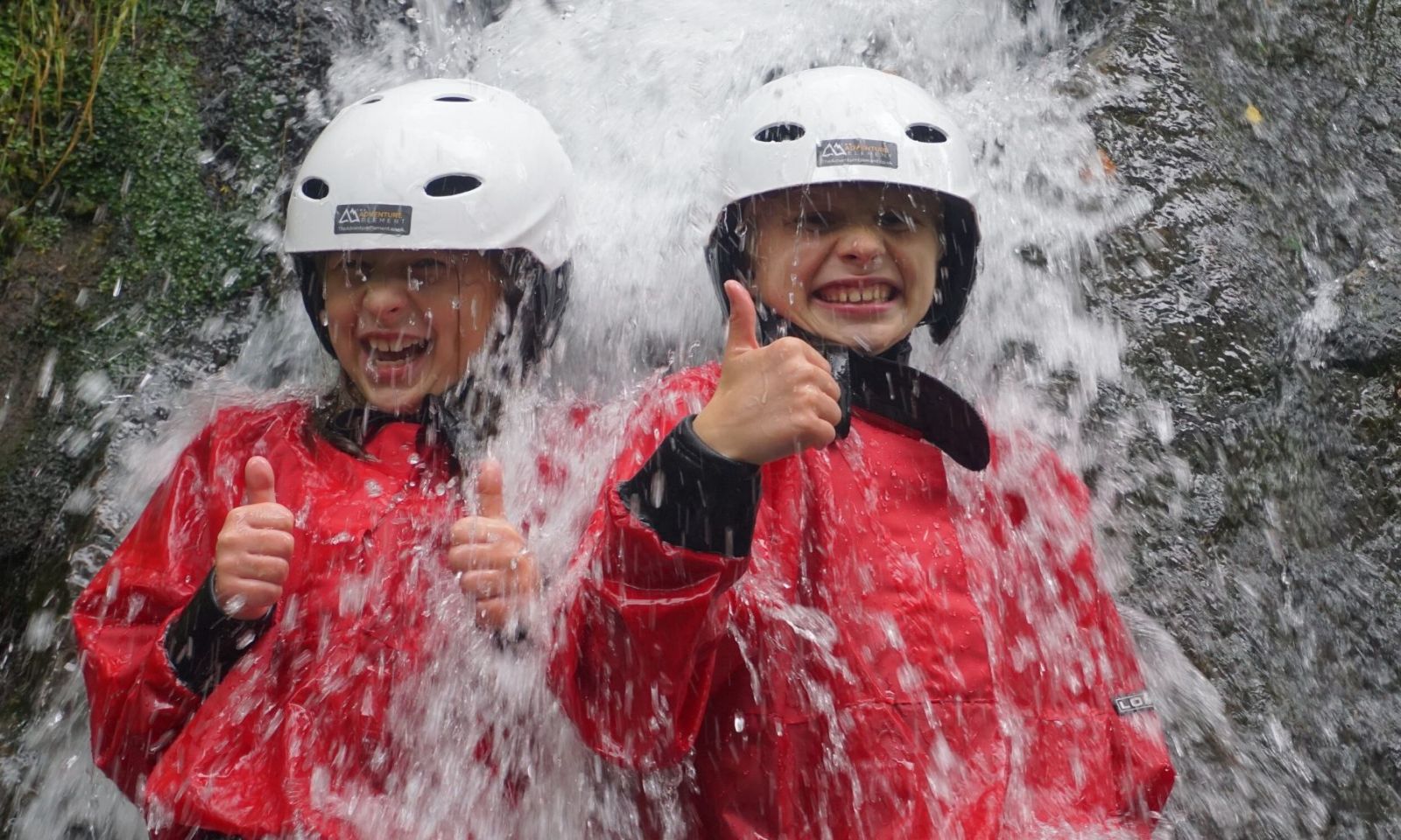 2 young boys lying in a waterfall with their thumbs up and laughing on a Ghyll scramble.