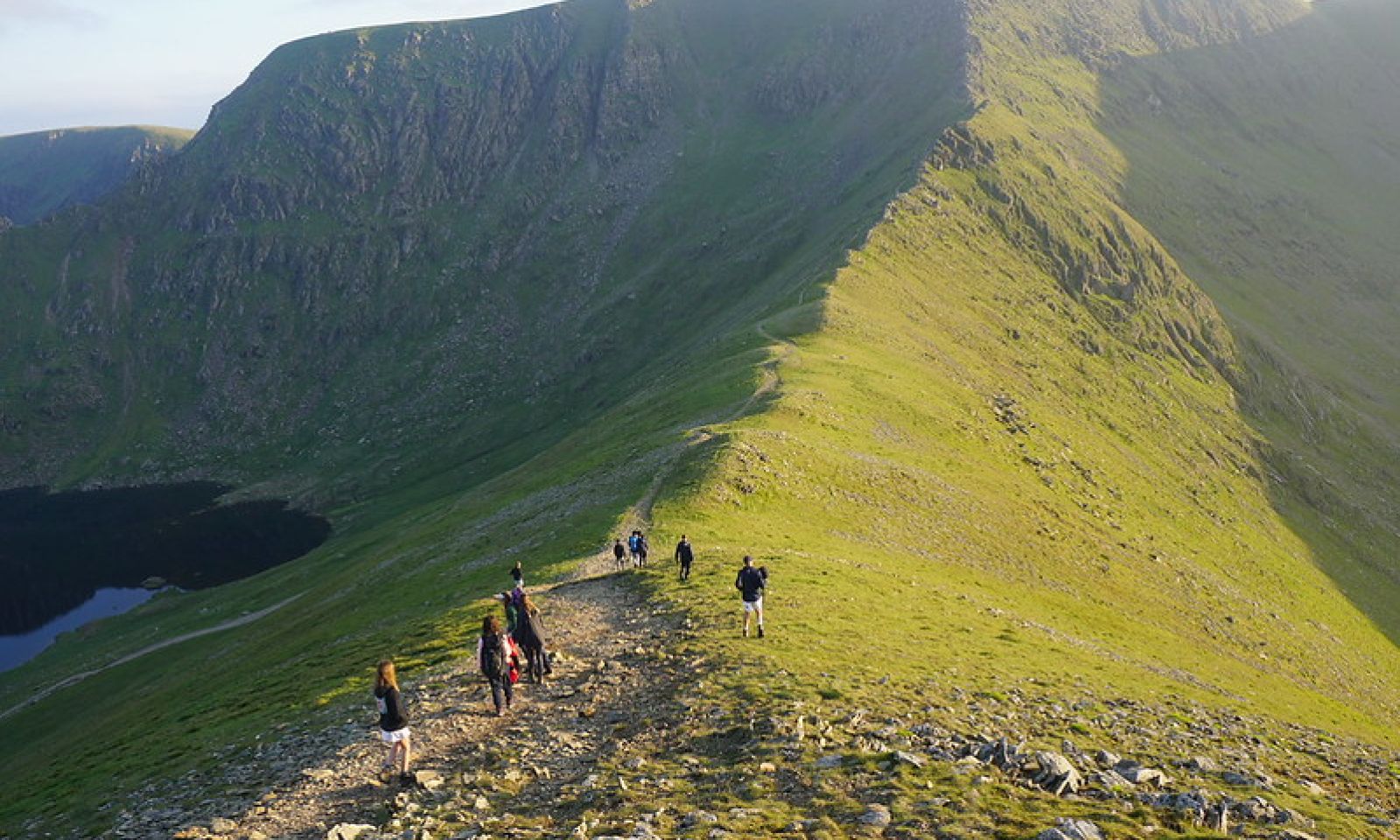 Young people walking up towards a mountain ridge with a tarn in the front