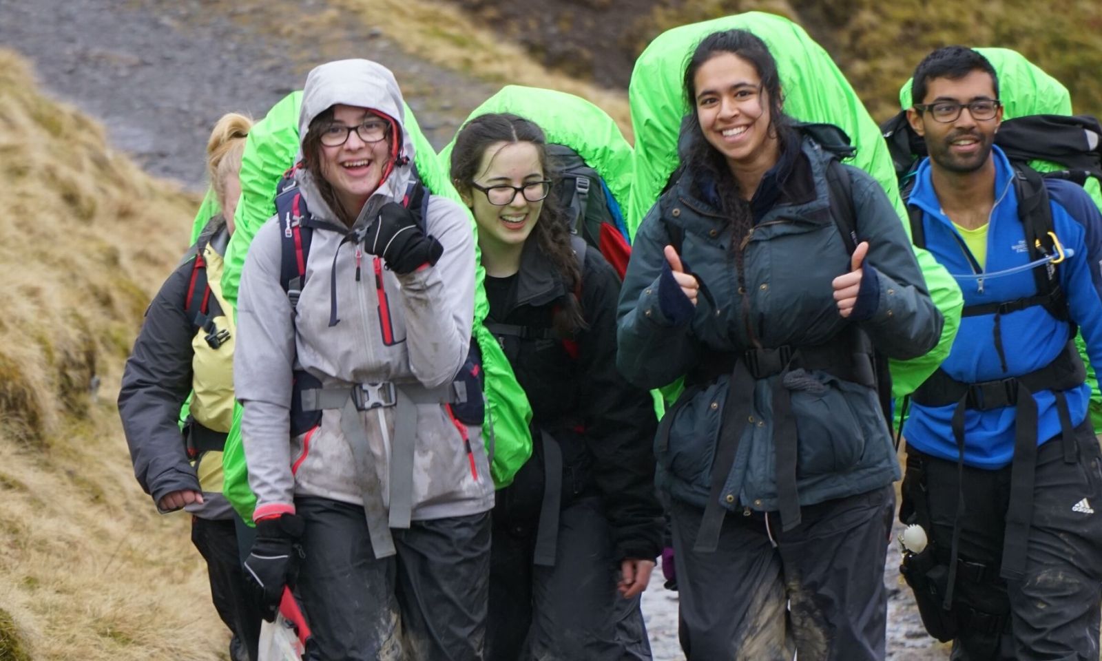 Group of 5 DofE participants on their expedition, walking with rucksacks and giving a thumbs up