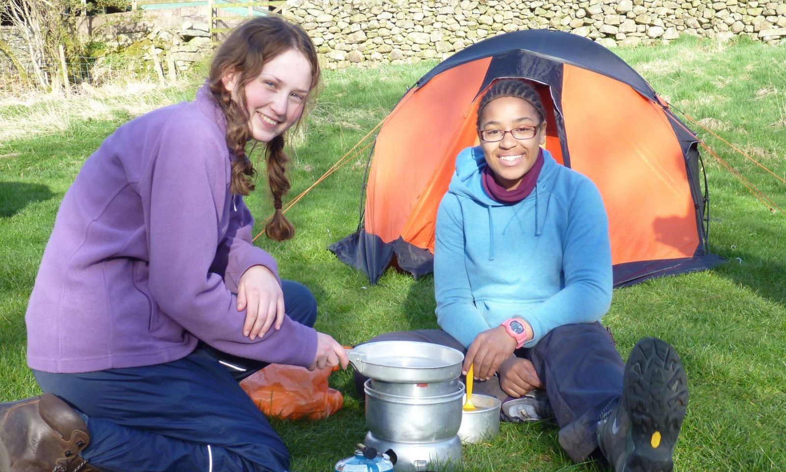 2 girls cooking on a stove and smiling on their DofE expedition.