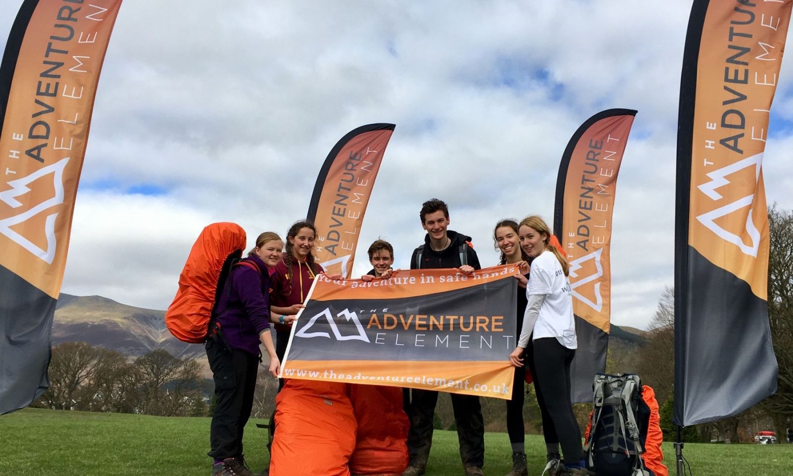 Group of DofE participants stand in front company flag and holding The Adventure Element flag.